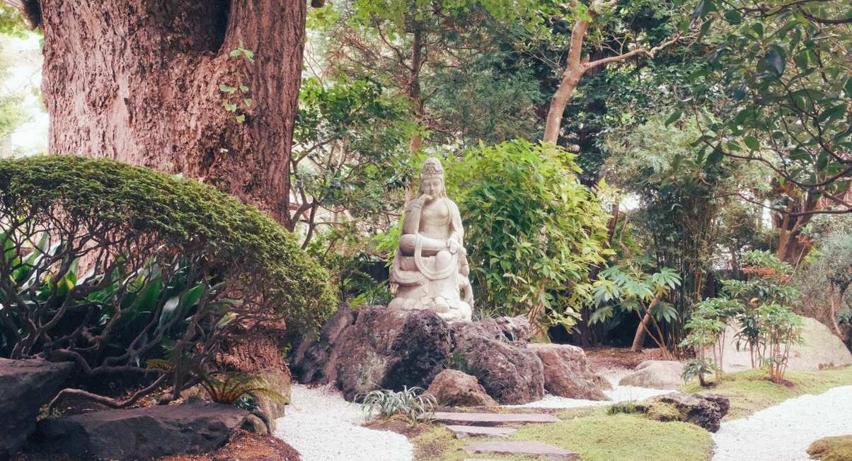 Jardin zen exterieur avec statue de pierre allee de gravier et vegetation luxuriante