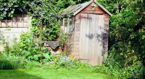 Cabane en bois au bardage grisé entourée de grimpantes et de massifs fleuris